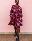 The model is wearing  merlot red, brown, red , coral and white abstract line print dress