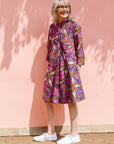 Model wearing a pink dress with floral yellow, blue and white print.