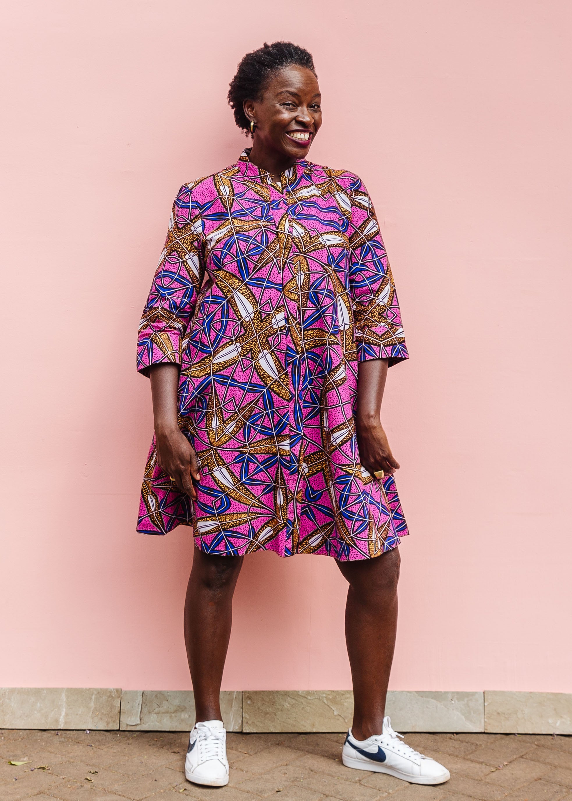 Model wearing a pink dress with floral yellow, blue and white print.