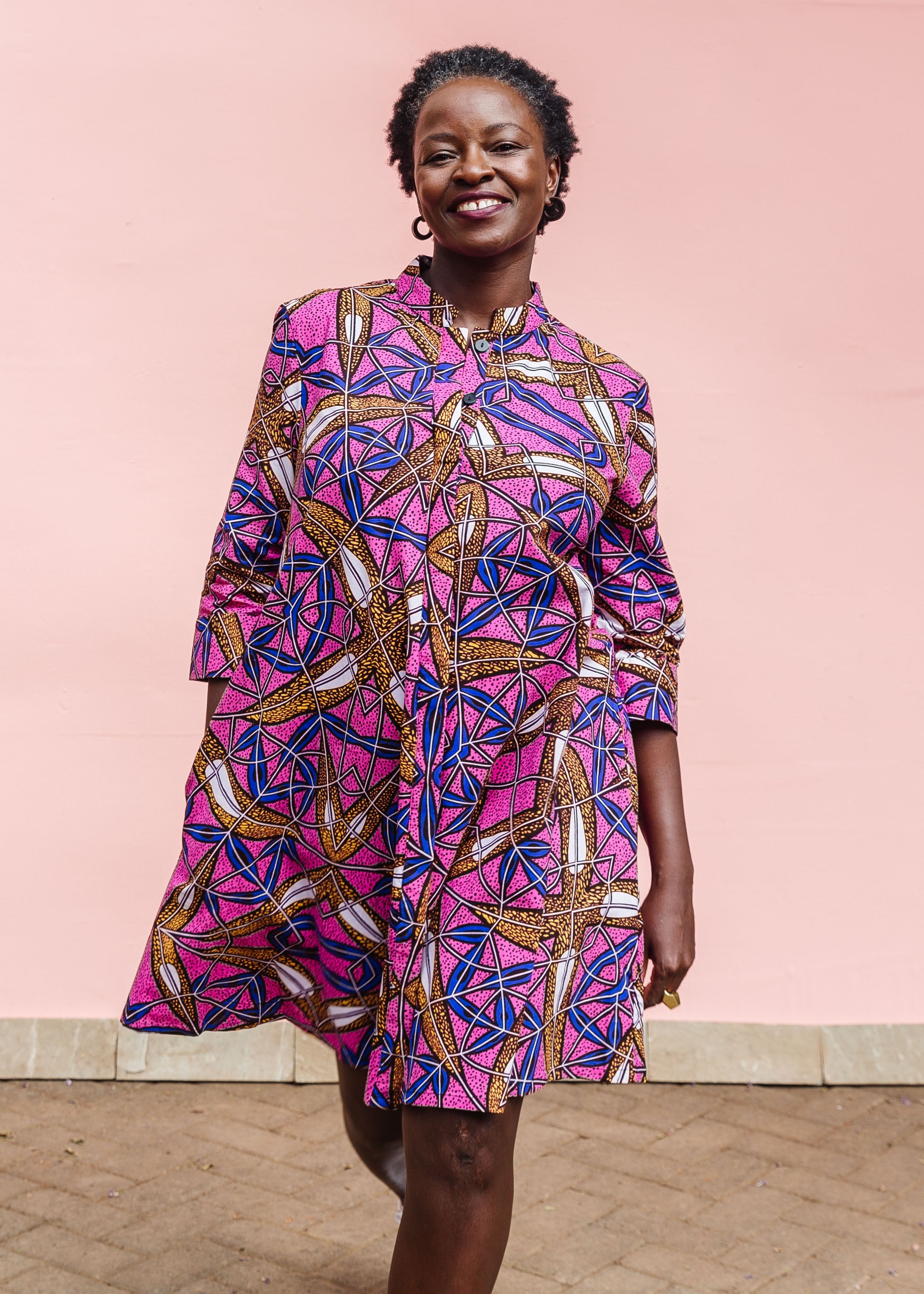 Model wearing a pink dress with floral yellow, blue and white print.