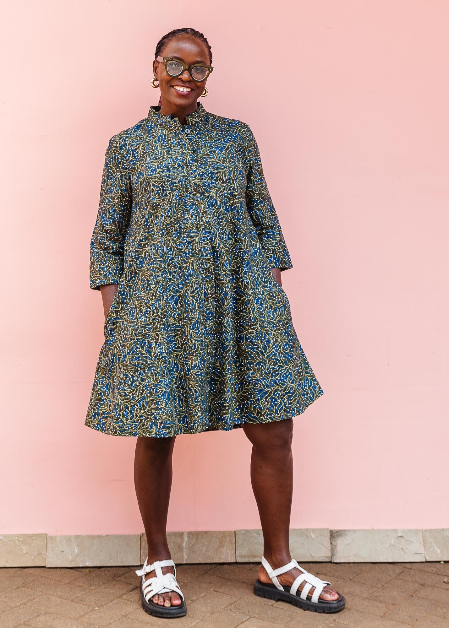 The model is wearing blue, white, black , yellow and green vine print dress