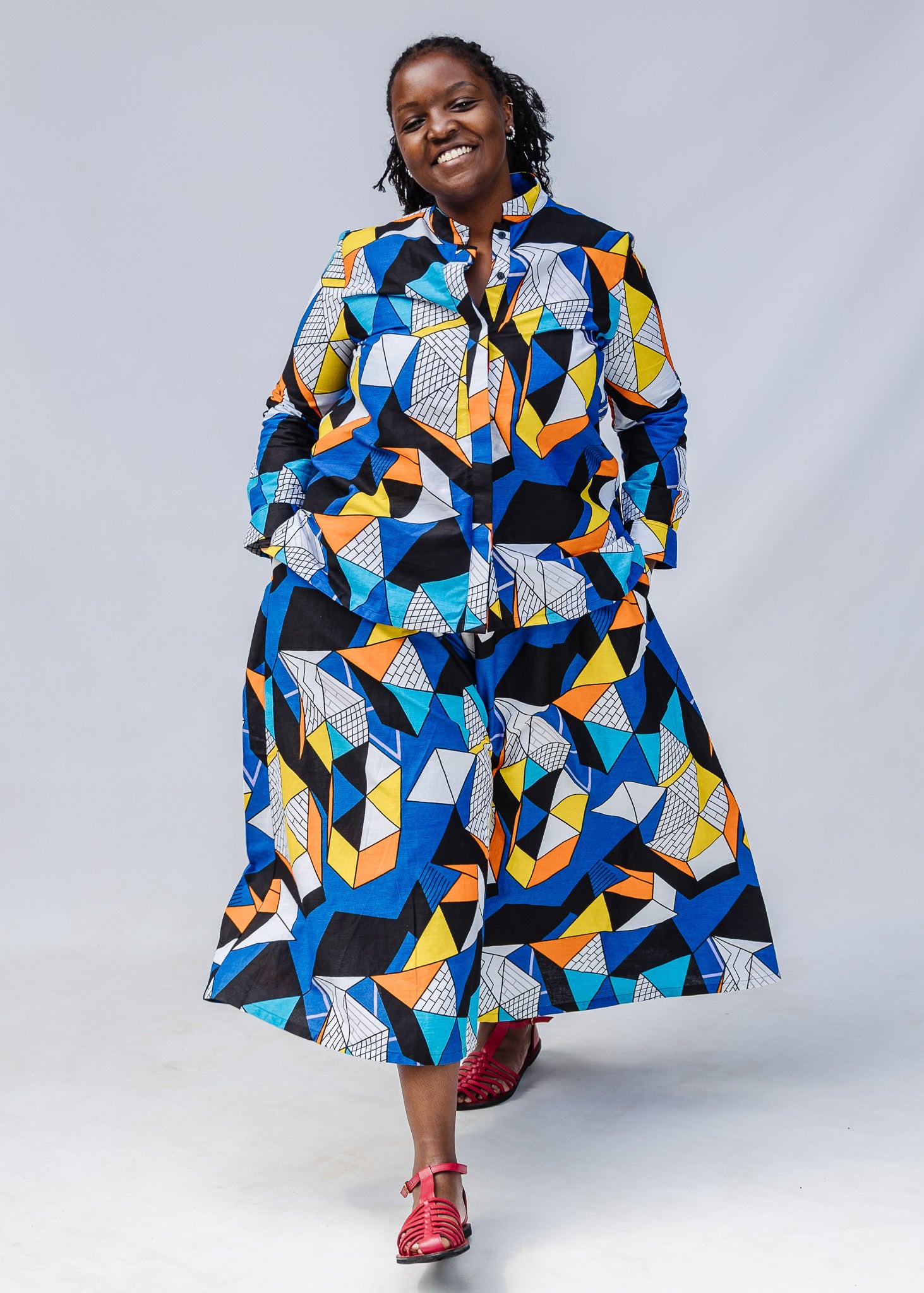 Model wearing blue, black, orange, yellow, orange and white geometric print shirt and culotte.