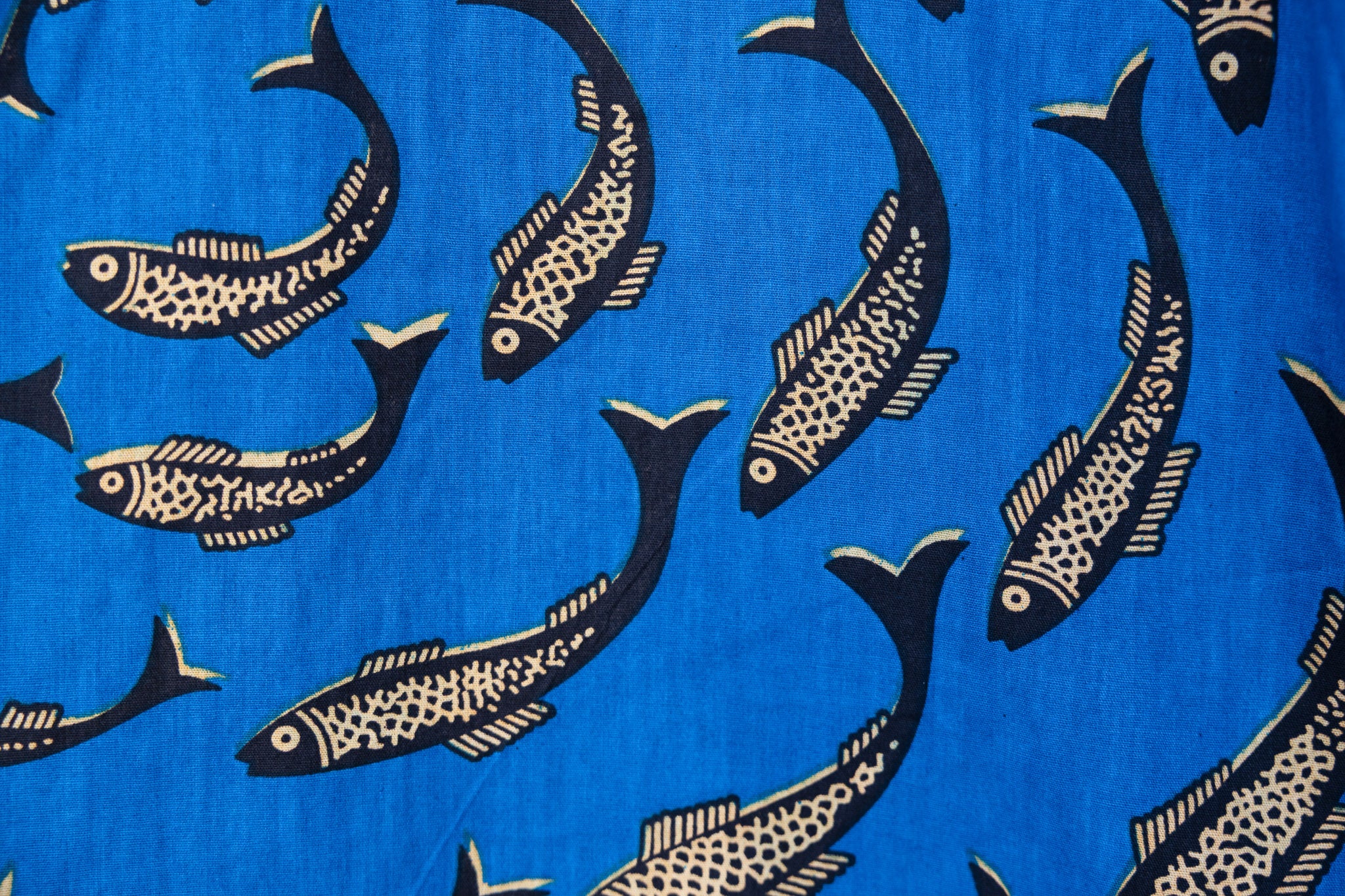 Close up display of blue pants with beige fish print, fabric.