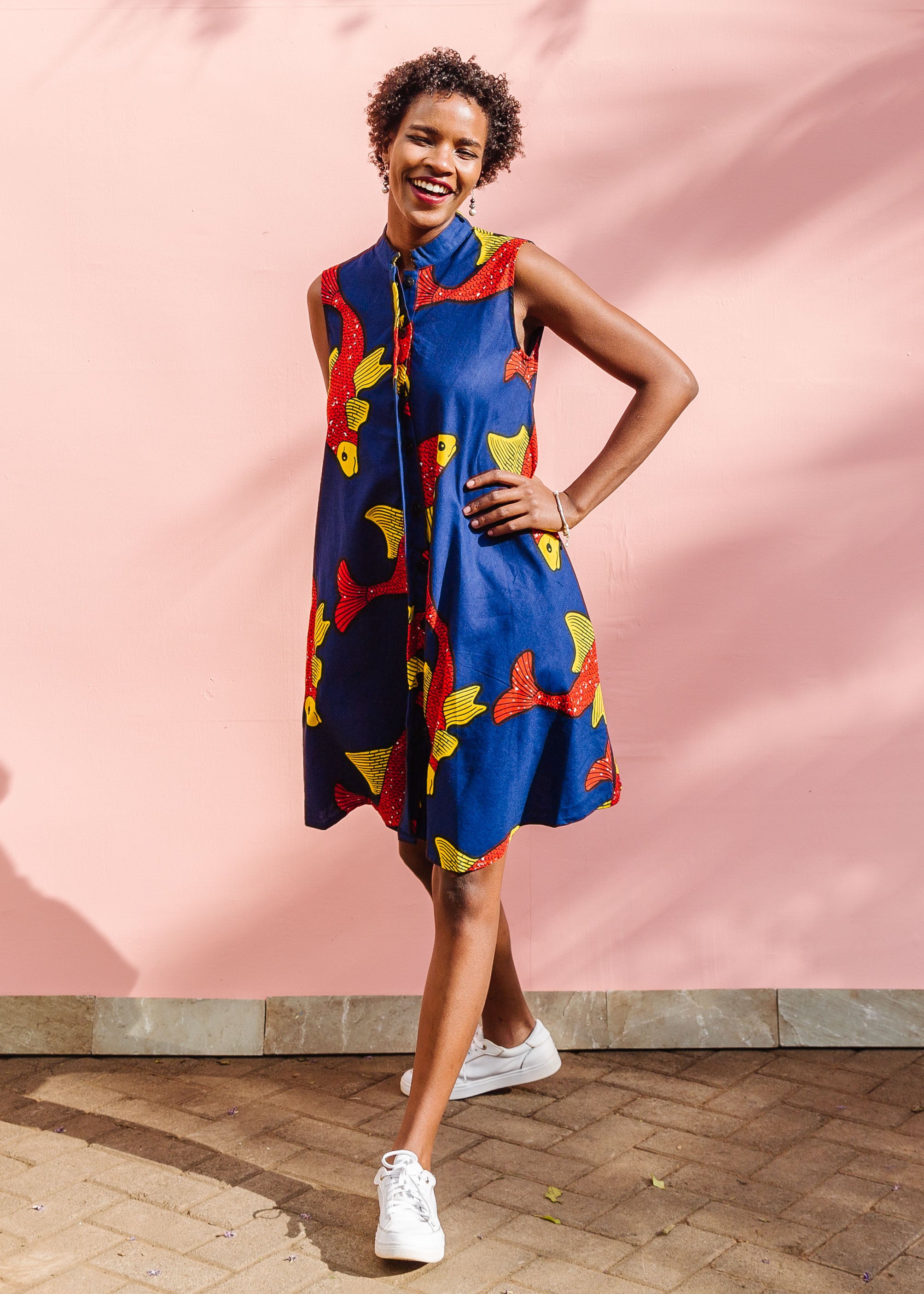 Model wearing navy sleeveless dress with red and yellow fish print.