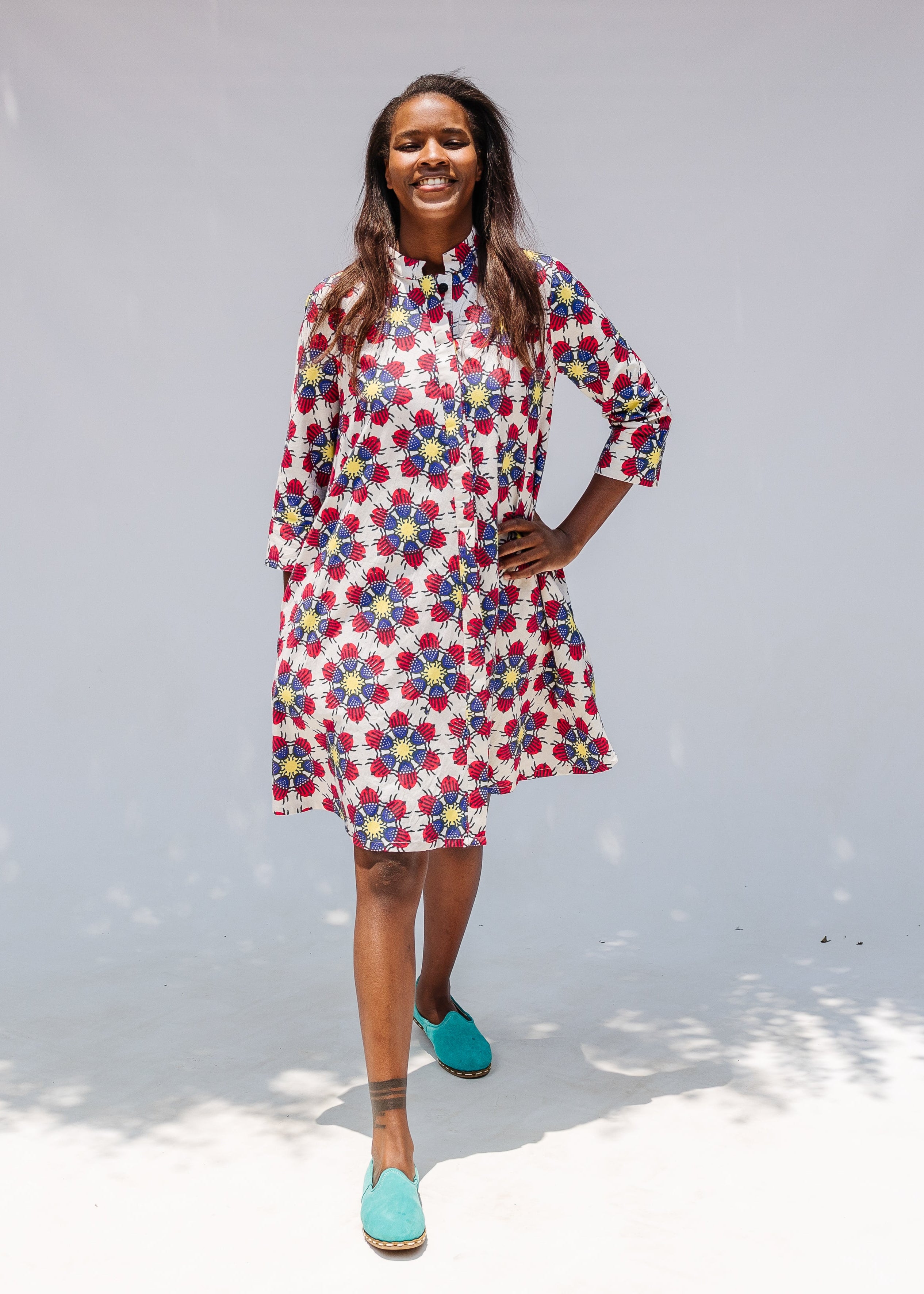 Model wearing white dress with yellow, red and blue bug print.