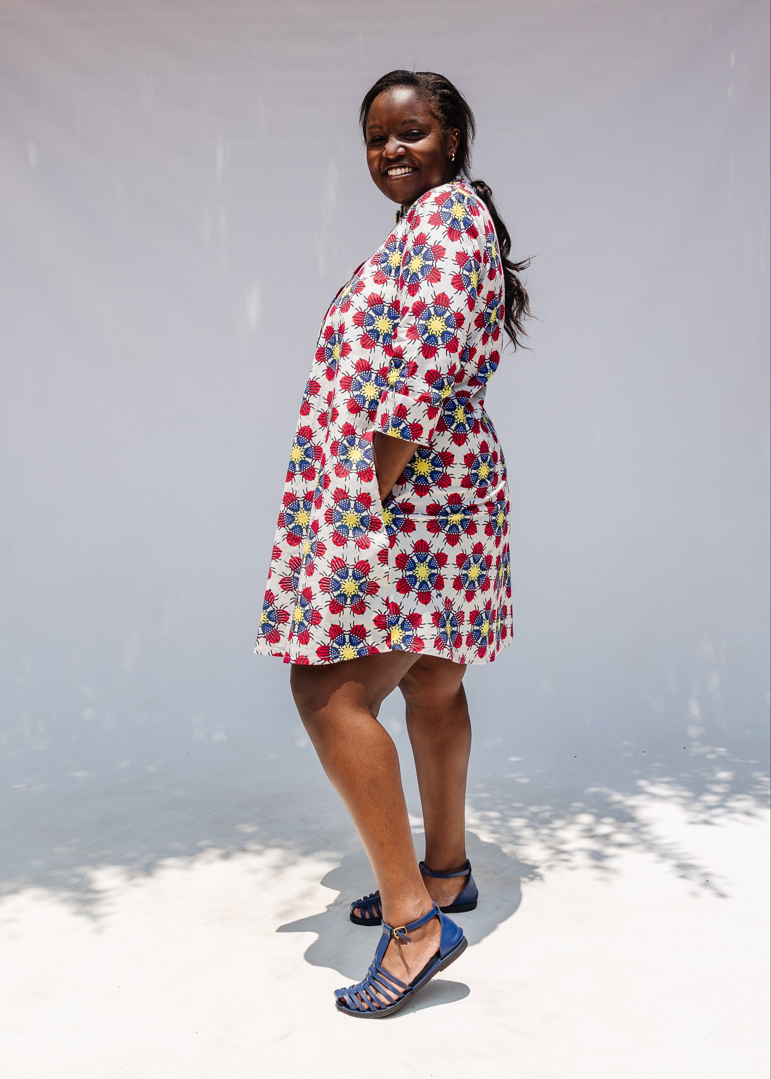 Model wearing white dress with yellow, red and blue bug print.