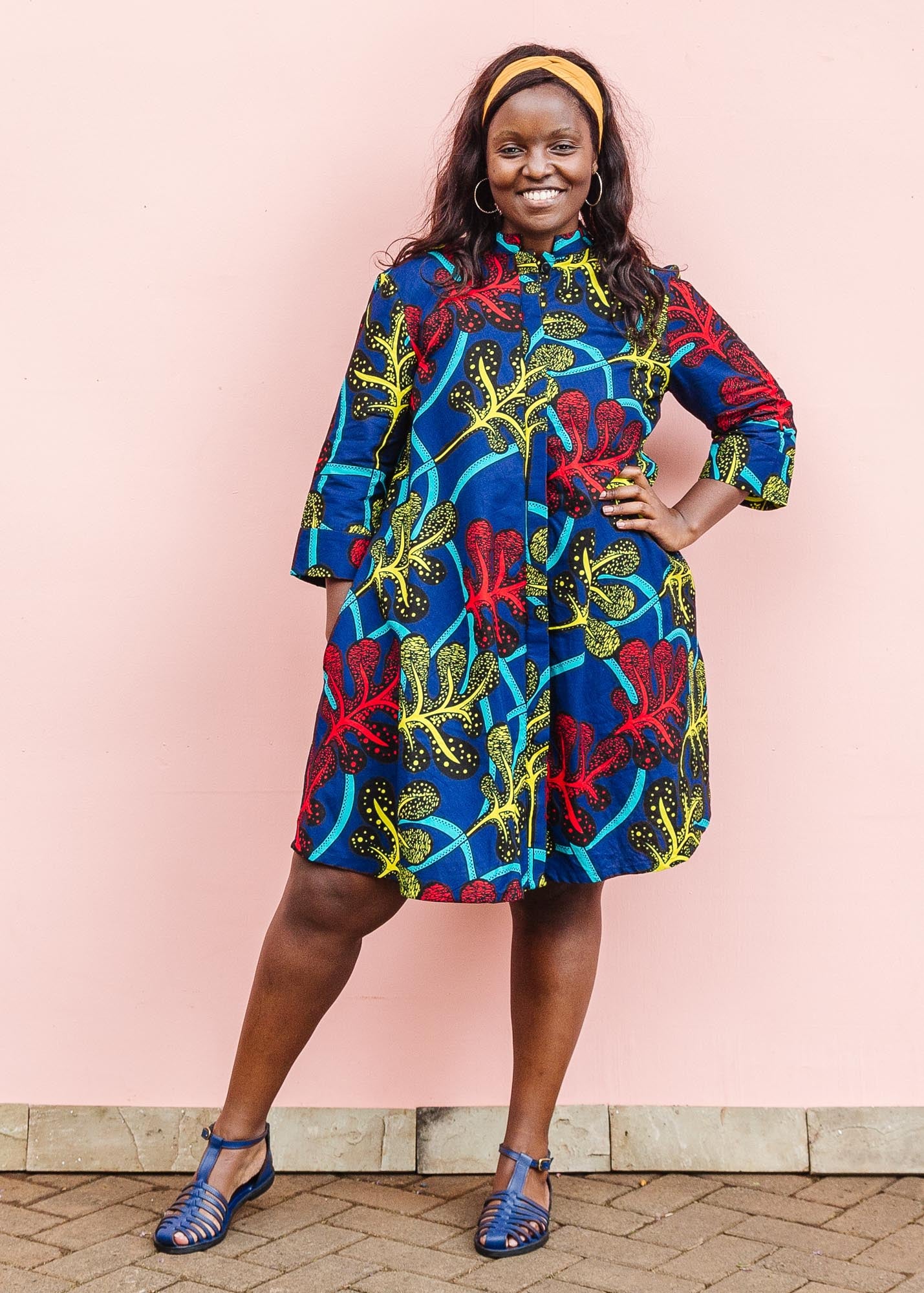 The model is wearing blue, red, yellow, black and aqua vine print dress