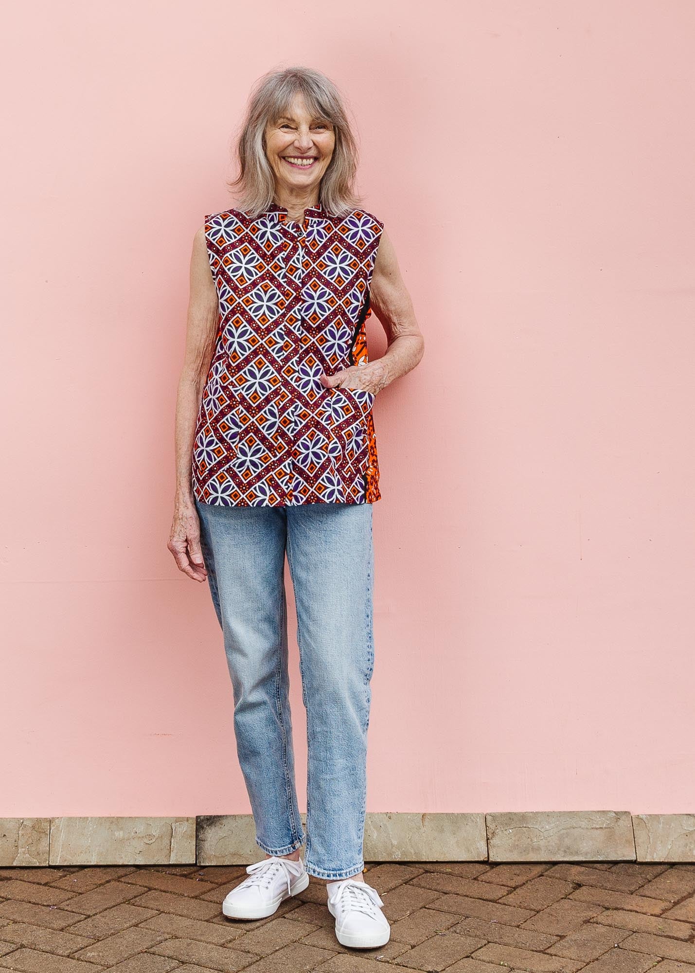 The model is wearing  orange, purple, white and black mixed pattern kanga tank