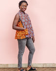 The model is wearing  orange, purple, white and black mixed pattern kanga tank