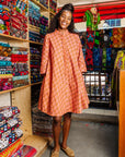 The model is wearing peach-pink, lavender and brown seashell print dress