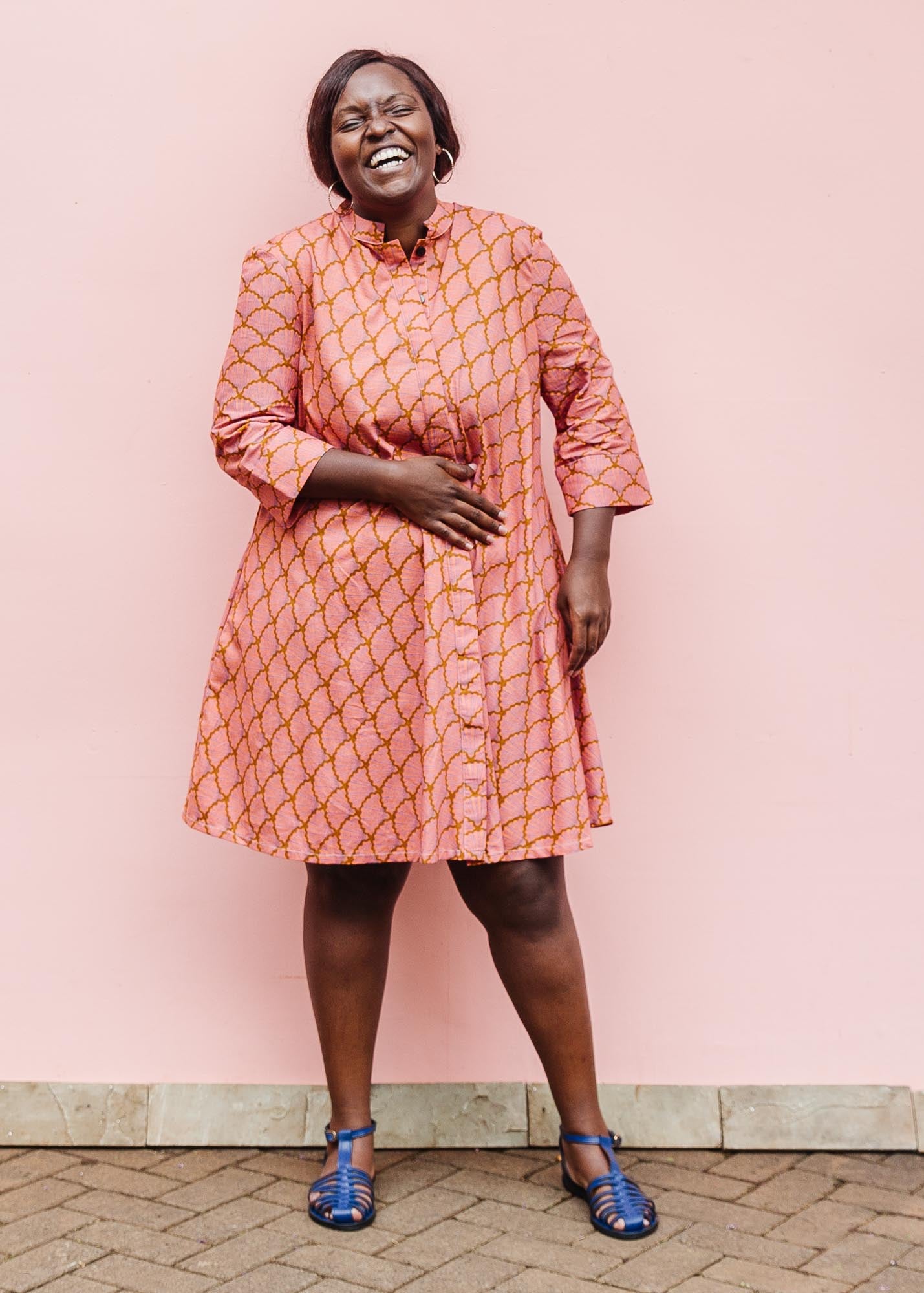 The model is wearing peach-pink, lavender and brown seashell print dress