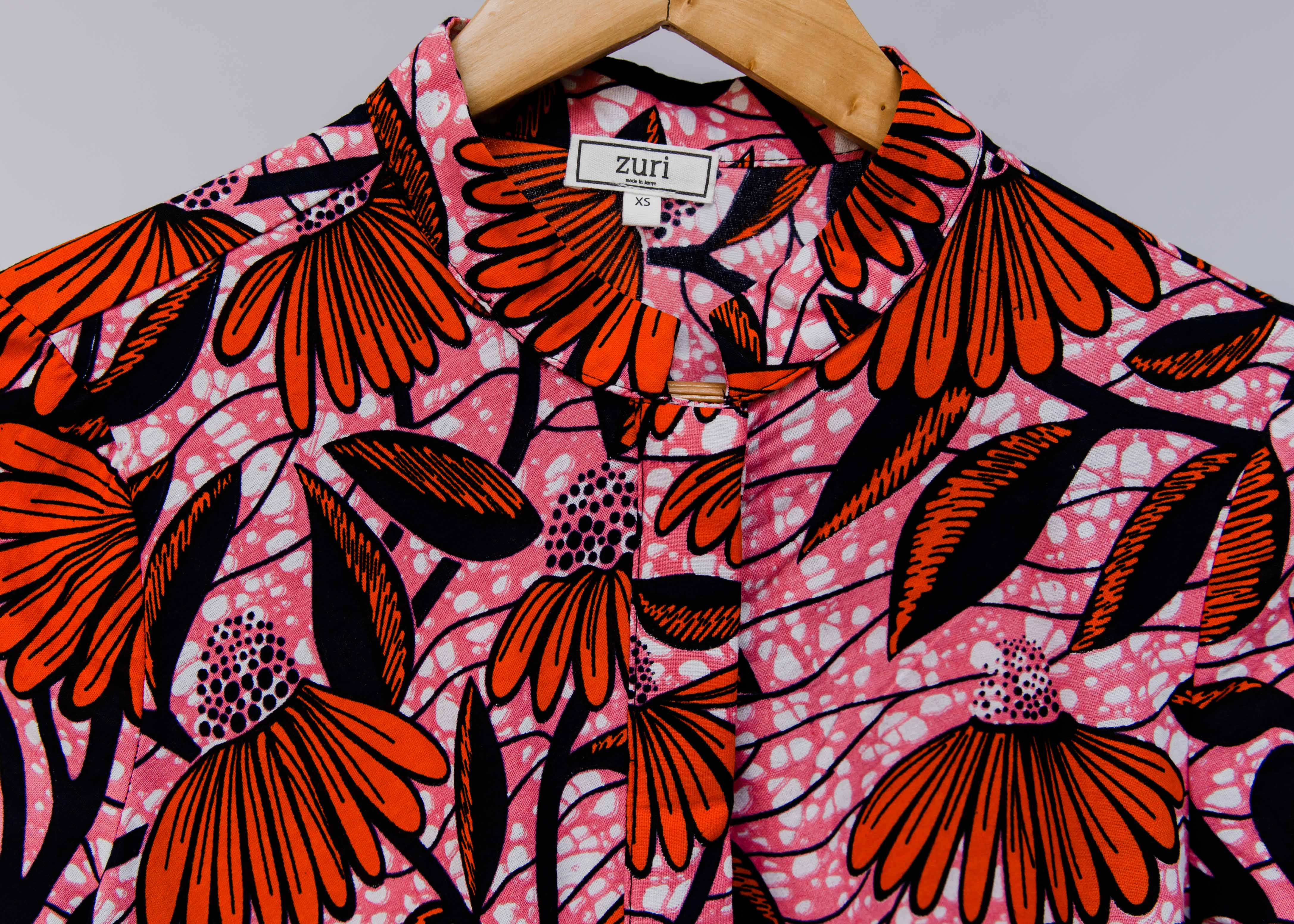 Close up display of pink dress with red and black flowers.