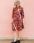 Model wearing pink dress with red and black flowers.