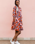 Model wearing pink dress with red and black flowers.