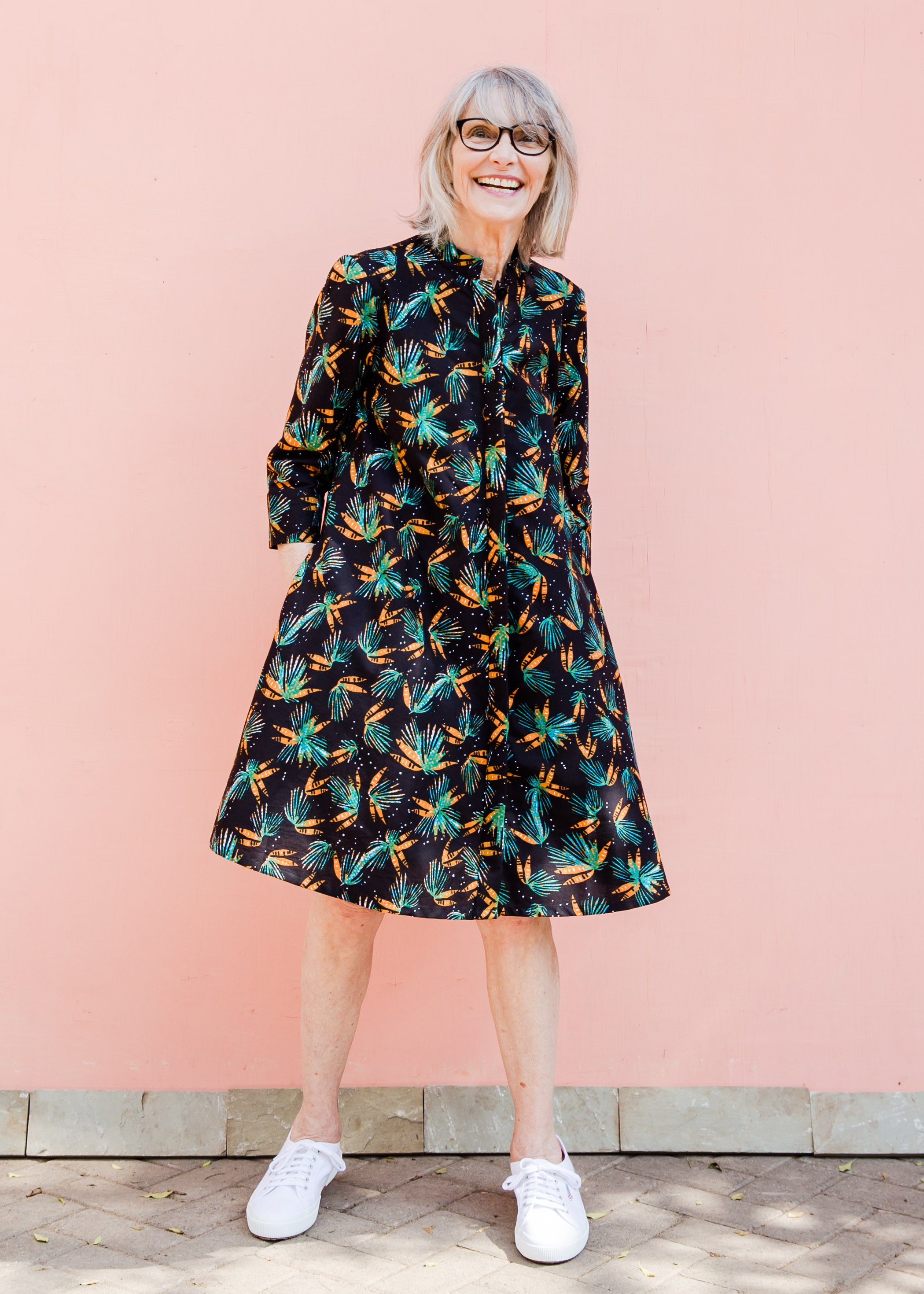 Model wearing black dress with teal and orange leaves with white dots.