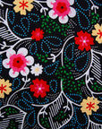 Close up display of black dress with white, green, red and yellow floral print, fabric.