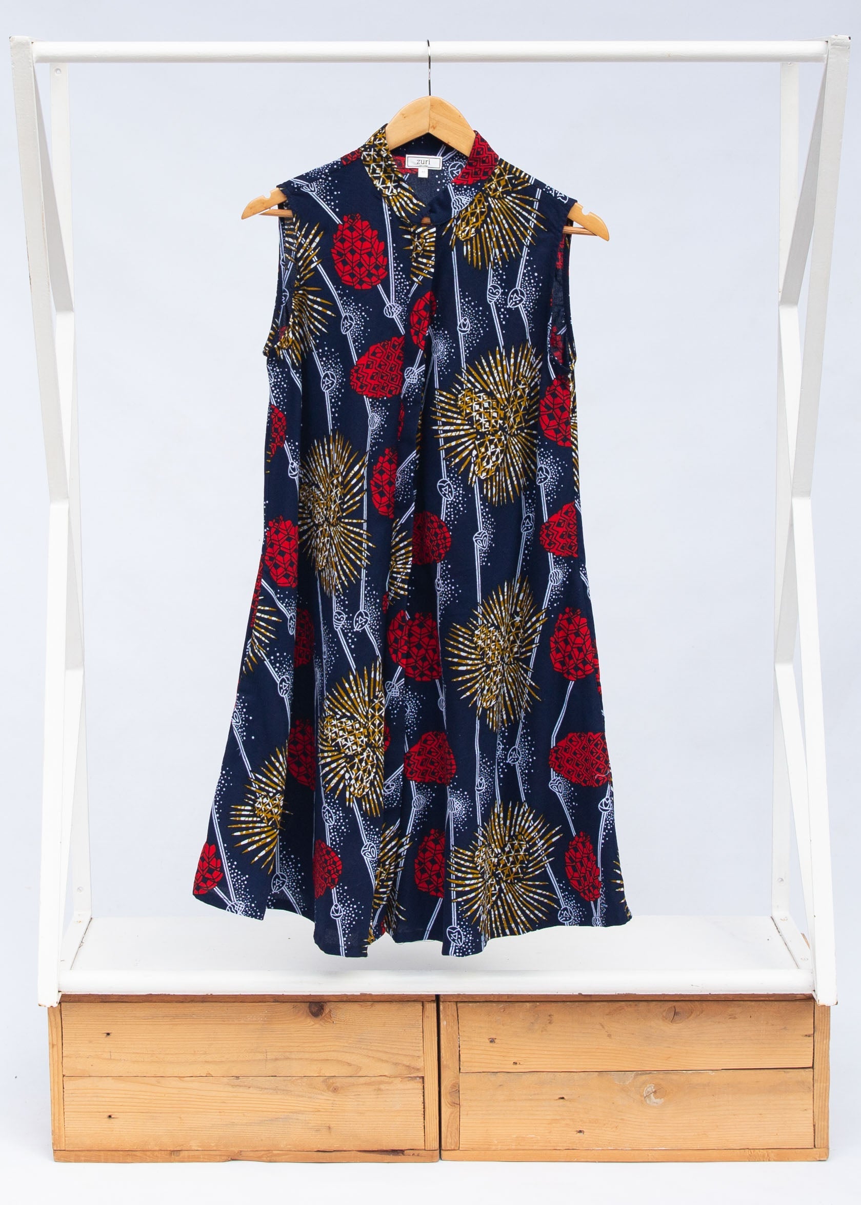 Display of navy sleeveless dress with red, yellow and white splatter print. 