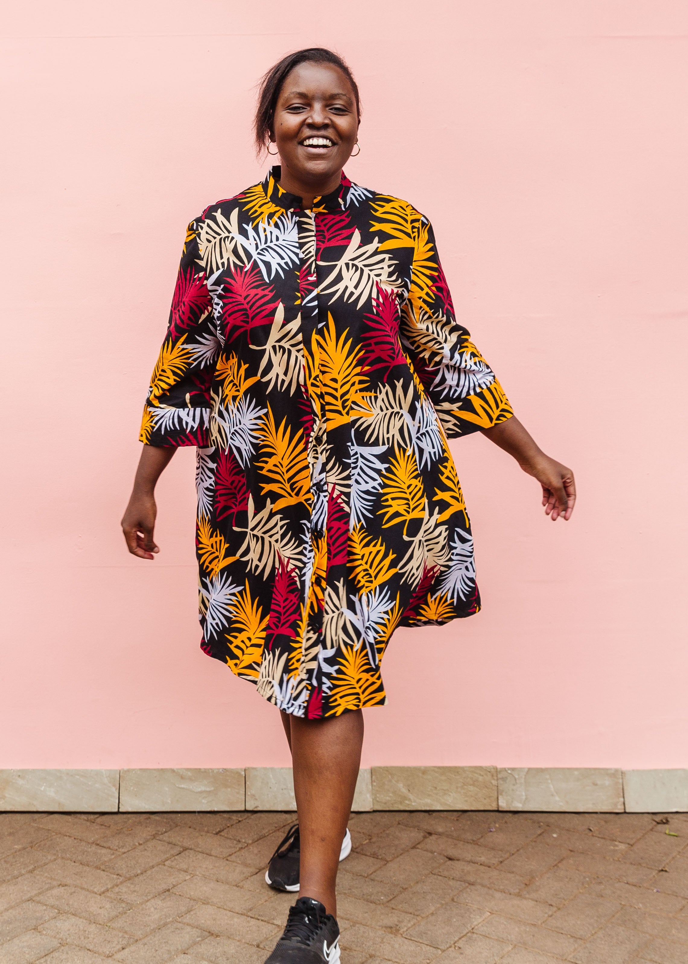 Model wearing black dress with orange, red and white leaf print.