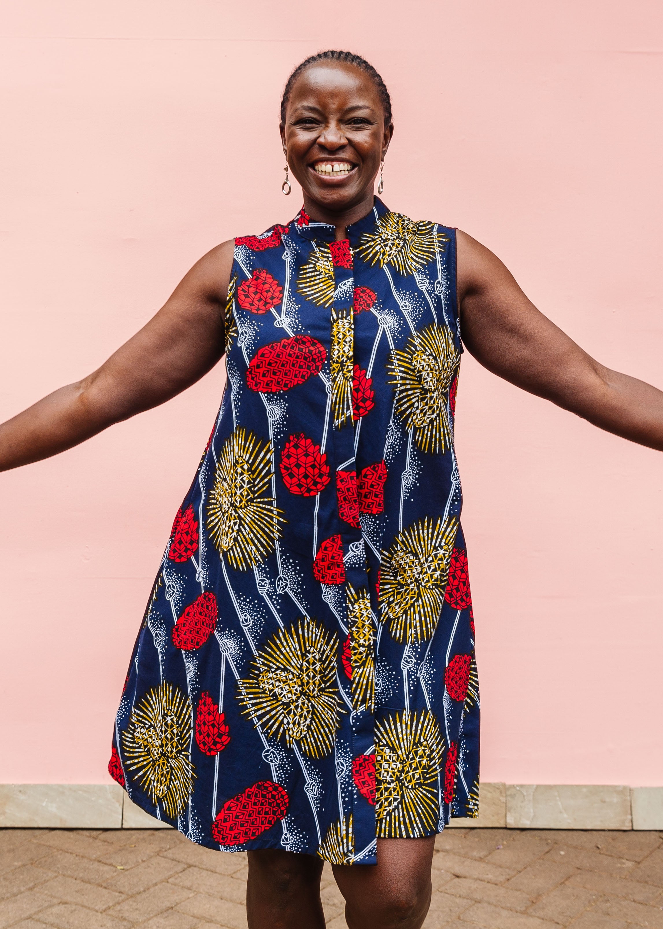 Model wearing navy sleeveless dress with red, yellow and white splatter print. 