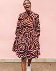 Model wearing brown, orange, burgundy and white abstract print dress.