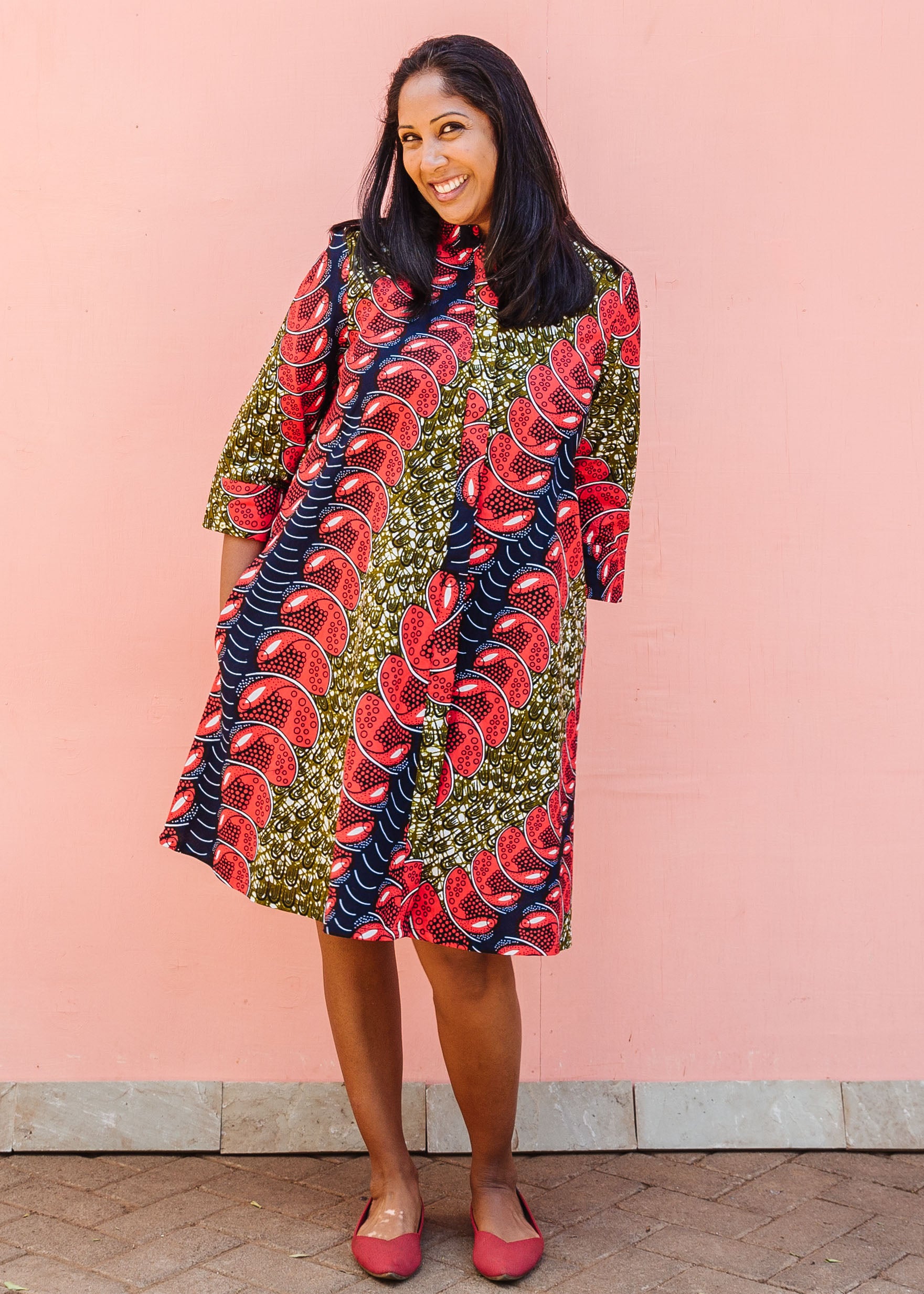 Model wearing green dress, with bold red and navy bauble print.