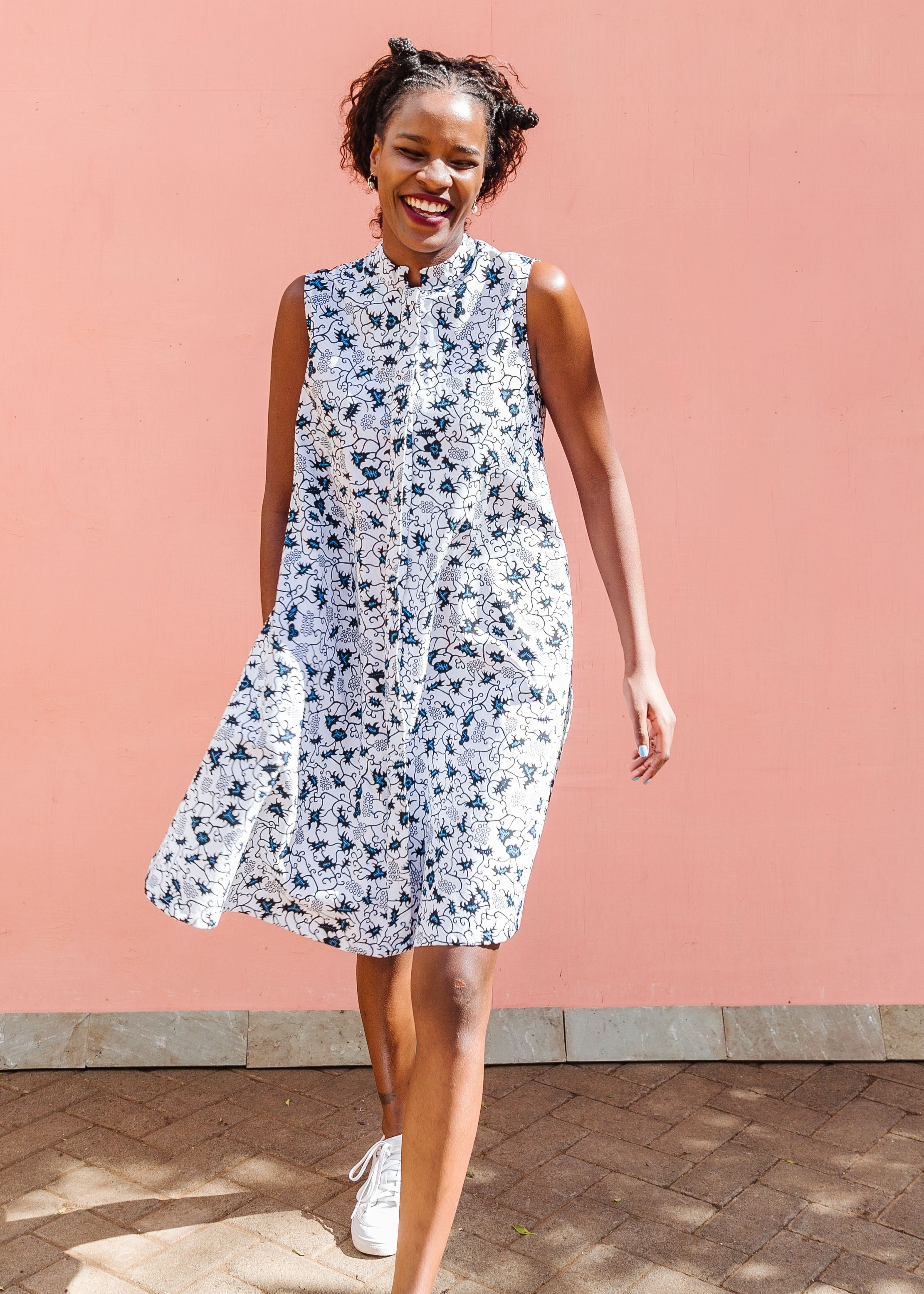 Model wearing white sleeveless dress with blue floral print.