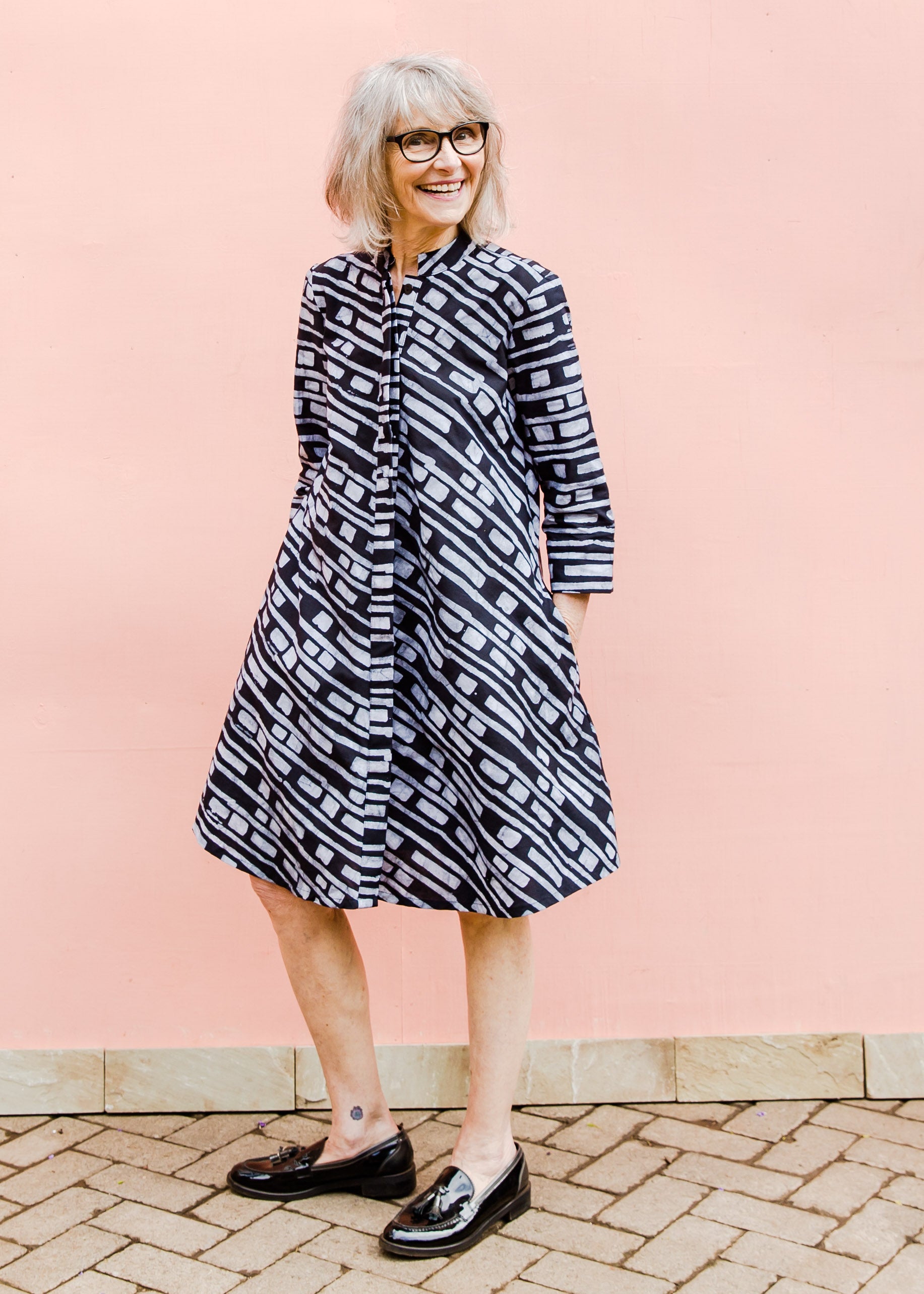 Model wearing dress with black and white line print, paired with black loafers.