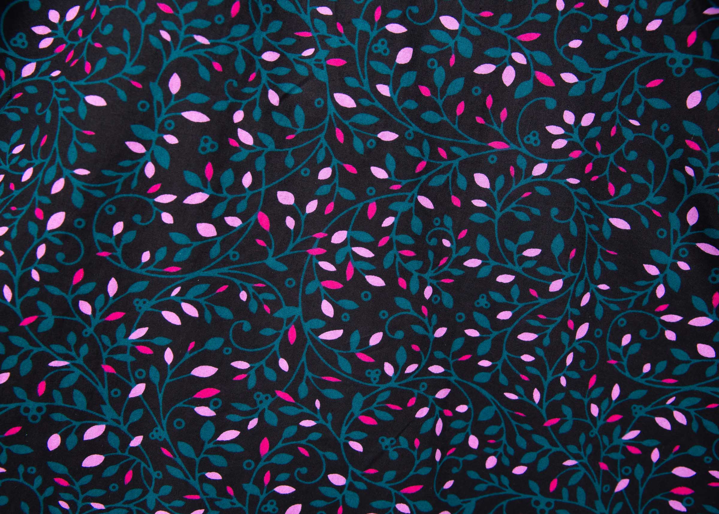 Close up display of black dress with teal and pink vine print, fabric.