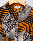 Display of black dress with orange stripes and black and white circles.