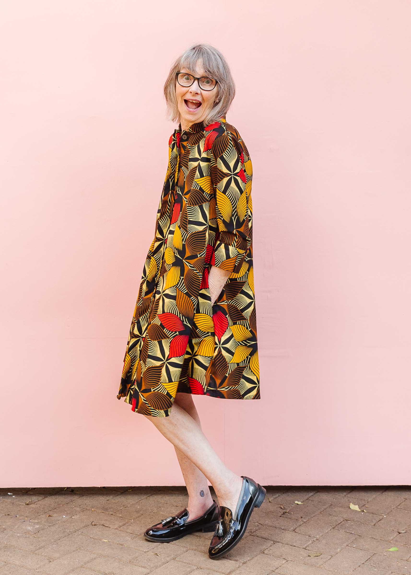 The model is wearing brown, yellow, red and black leaf print dress.